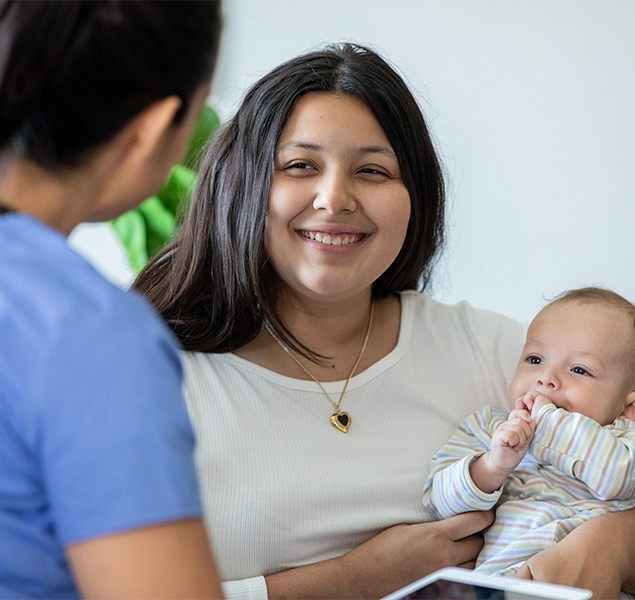 Young mother holding her infant and speaking to a home visitor