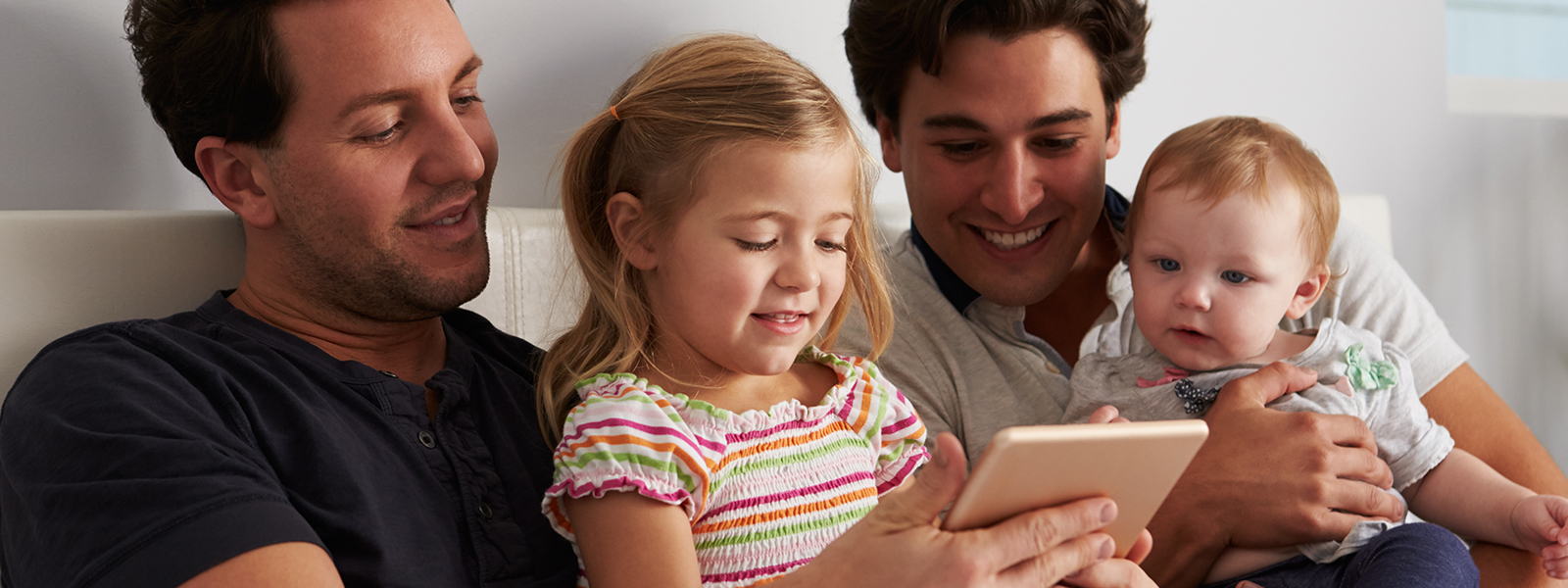 male gay parents with children sitting on their lap and reading to their children